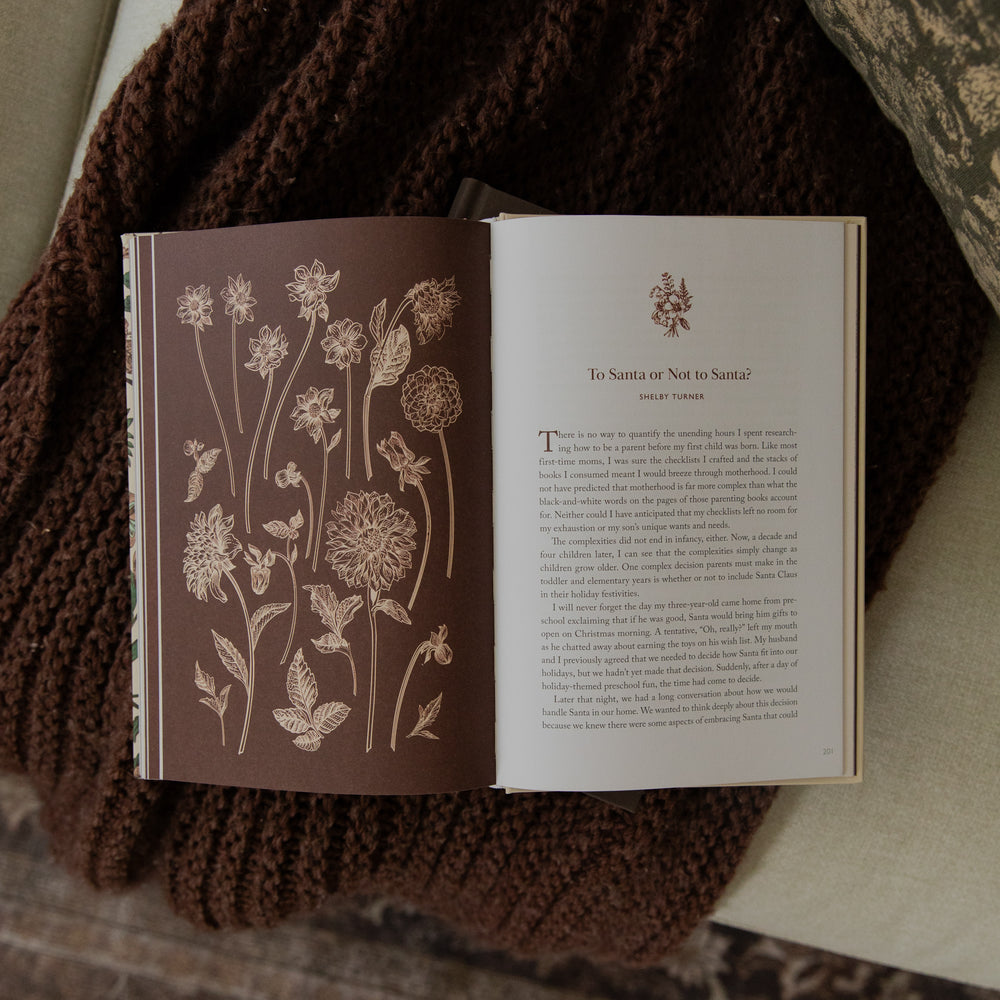 An open book laid on a brown knitted blanket, showing a floral illustration on the left page and a text page titled 'To Santa or Not to Santa' on the right.