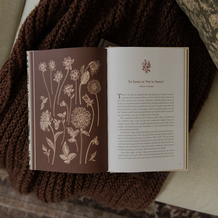 An open book laid on a brown knitted blanket, showing a floral illustration on the left page and a text page titled 'To Santa or Not to Santa' on the right.