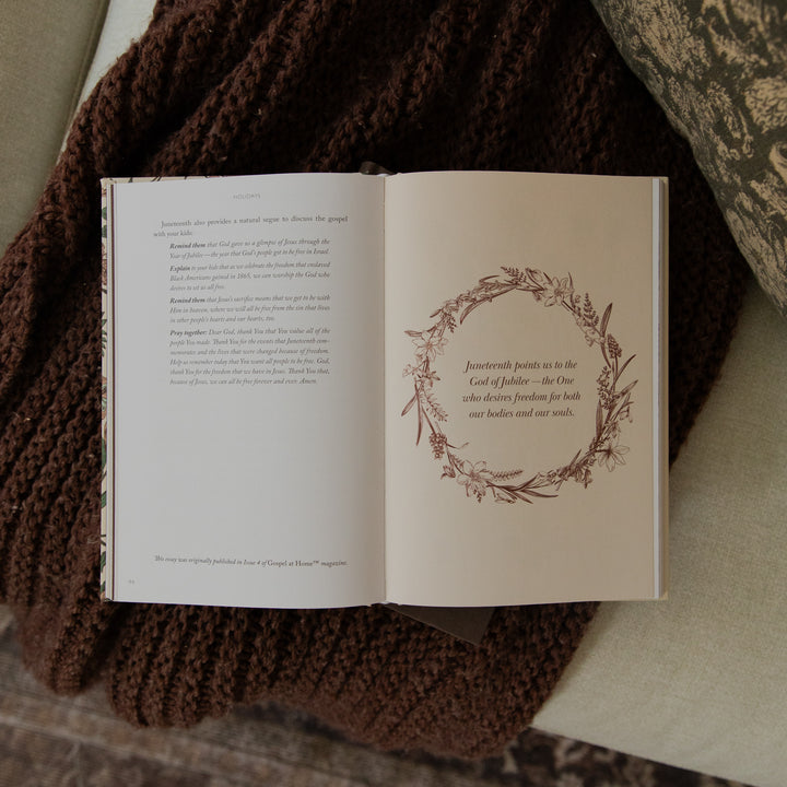 An open book laid on a dark brown chunky knit blanket, showing printed text on the left page and a decorative wreath illustration with a quote on the right page.