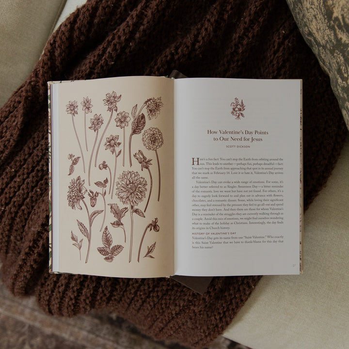 An open book with floral line drawings on the left page and a poem titled 'How Valentine's Day Ends, to Our Need for Joy' on the right page, styled on a beige surface with a brown knitted blanket nearby.