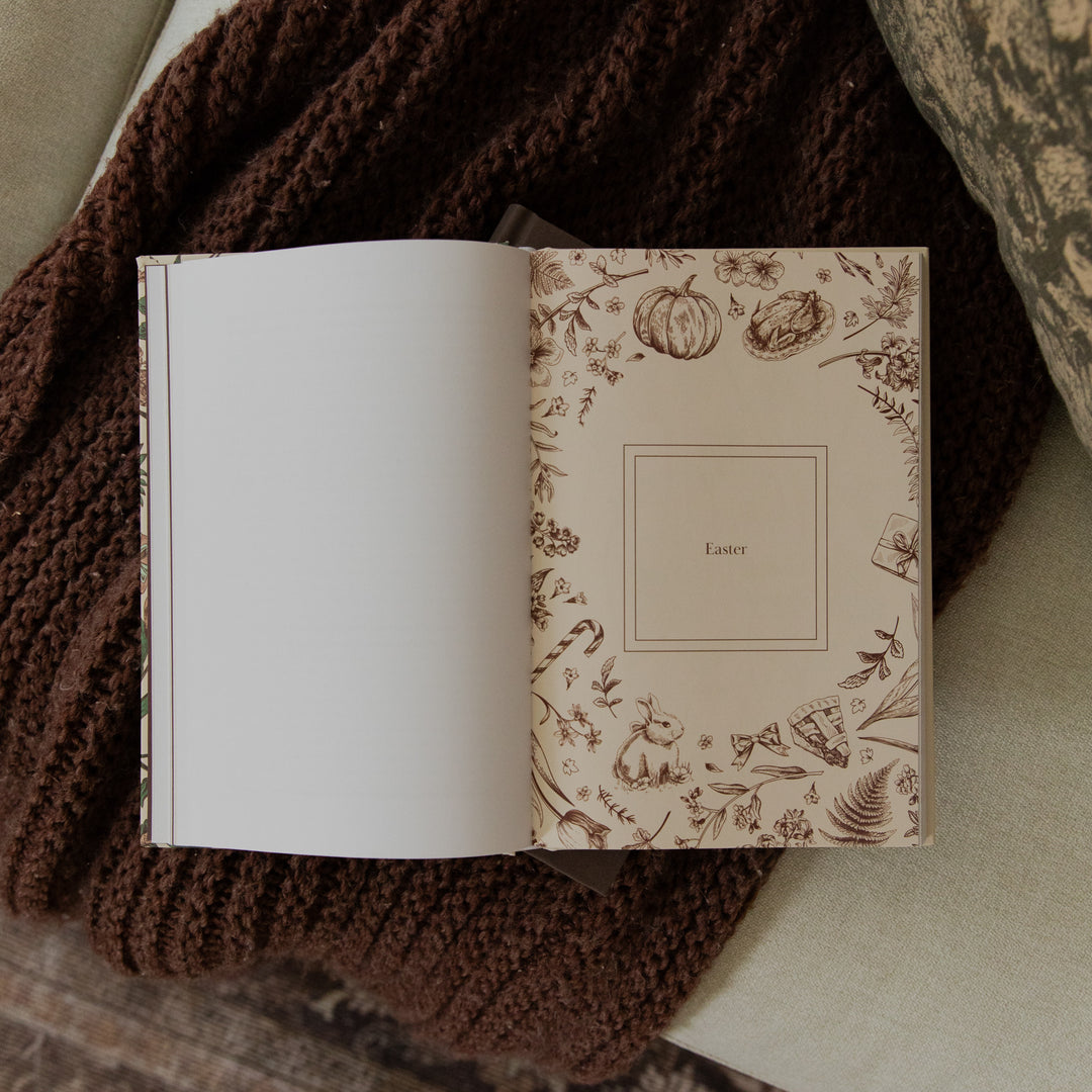 An open personalized book or journal resting on a chunky brown knit blanket. The right page features a cream-colored cover decorated with a brown botanical border illustration and the word 'Easter' in the center, while the left page is blank.