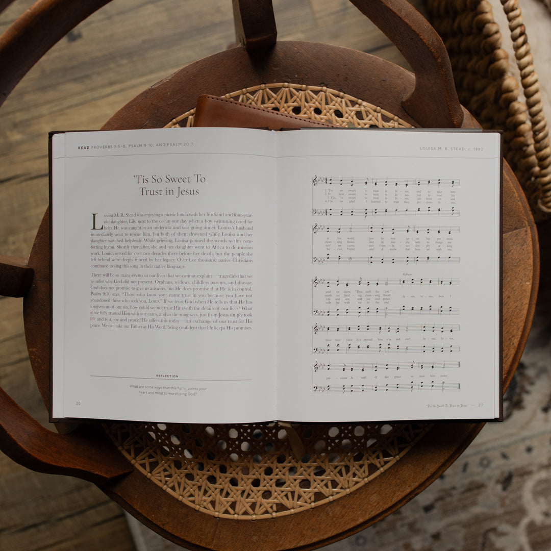 The I need Thee Every Hour book opened to the Tis so Sweet to trust in Jesus page on a wicker chair