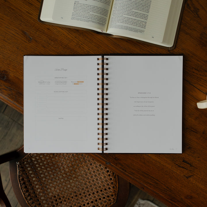 Identity in Christ Verse Map Journal opened to a Verse Map page on a wooden table near a coffee mug and an open bible