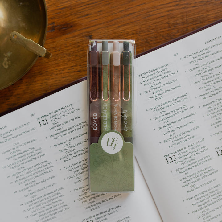 All four of the Identity Pen Set in the package on an open bible and on a wooden table