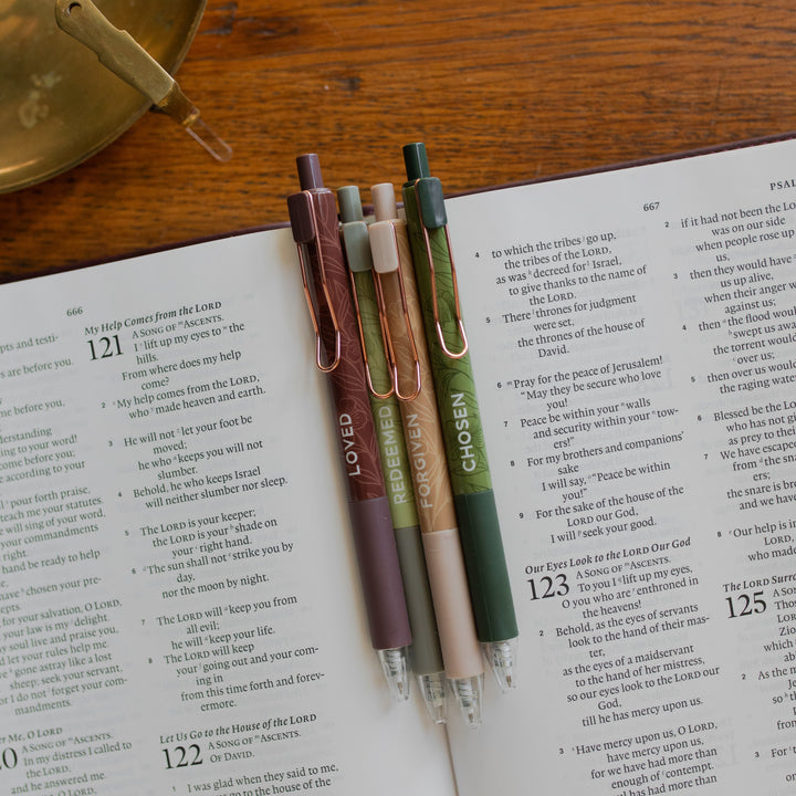 All four of the Identity Pen Set on an open bible and on a wooden table