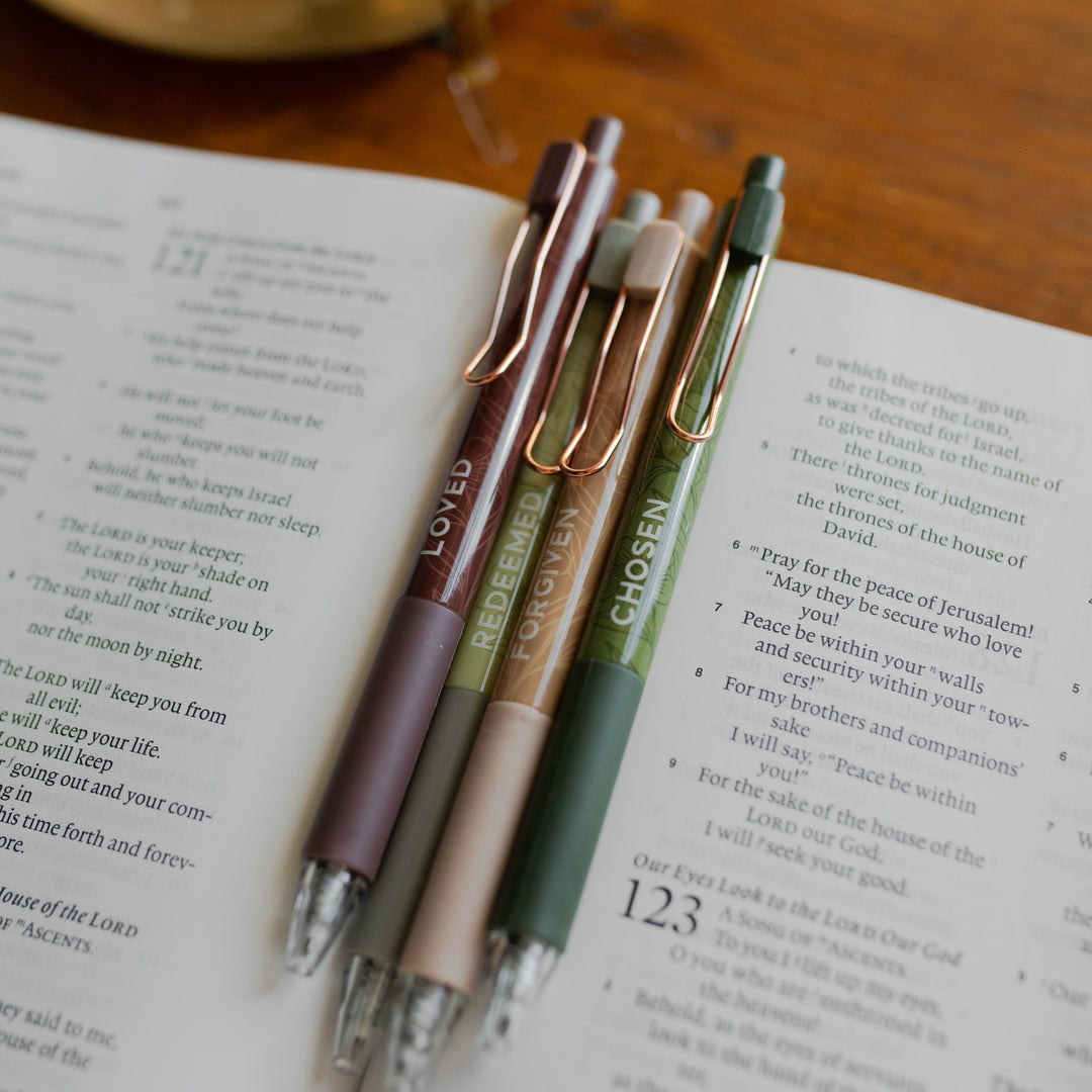 Up close of All four of the Identity Pen Set on an open bible and on a wooden table