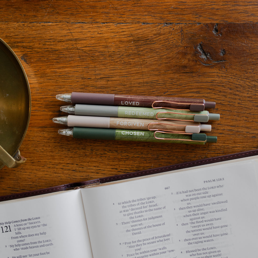 All four of the Identity Pen Set on a wooden table next to an open bible