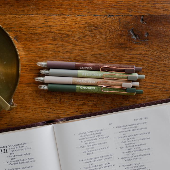 All four of the Identity Pen Set on a wooden table next to an open bible