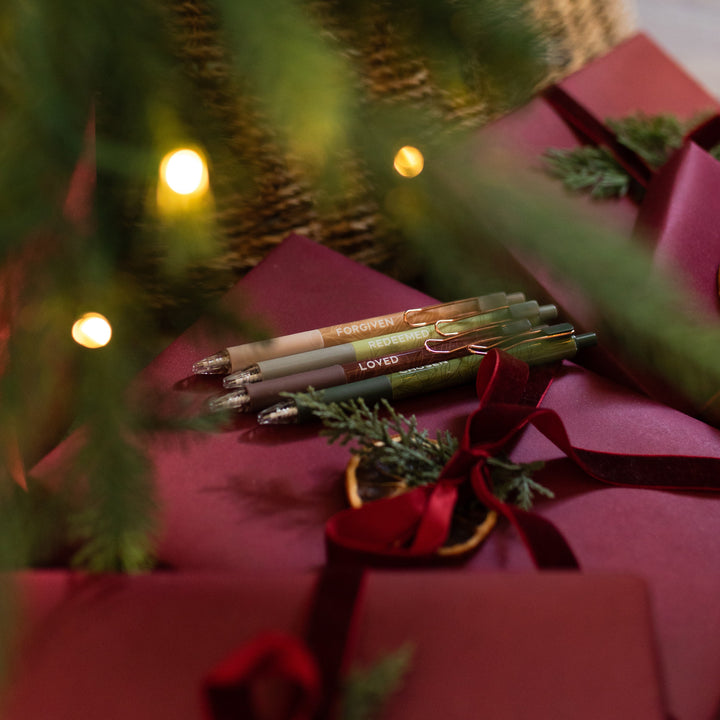 All four of the Identity Pen Set on an red package wrapped with a red ribbon and next to a green tree