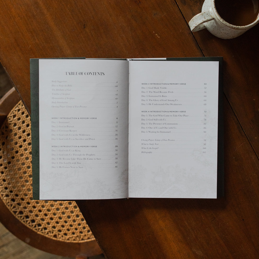The Immanuel Hardcover opened to the table of contents page on a wooden table next to a coffee cup