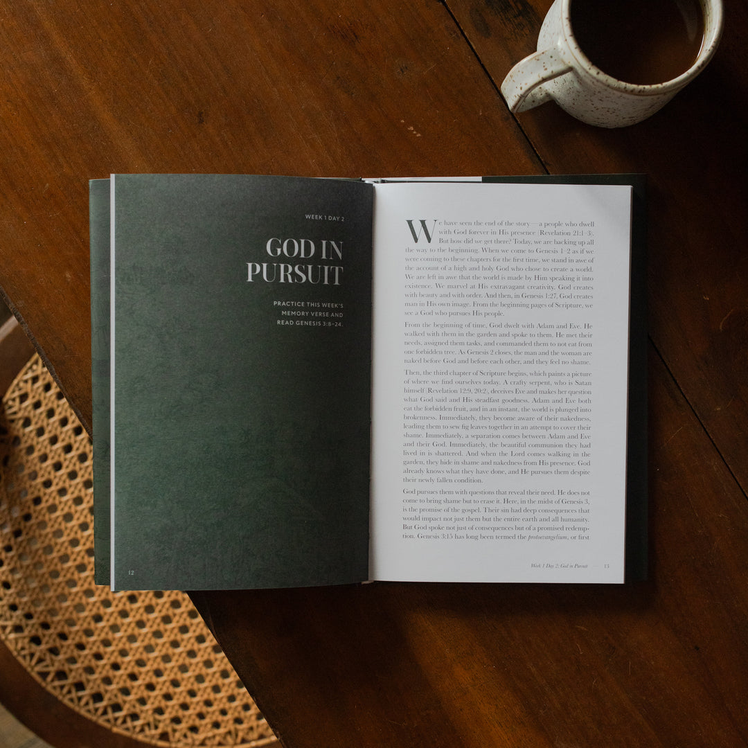 The Immanuel Hardcover opened to the Week 1 and Day 2 page on a wooden table next to a coffee cup