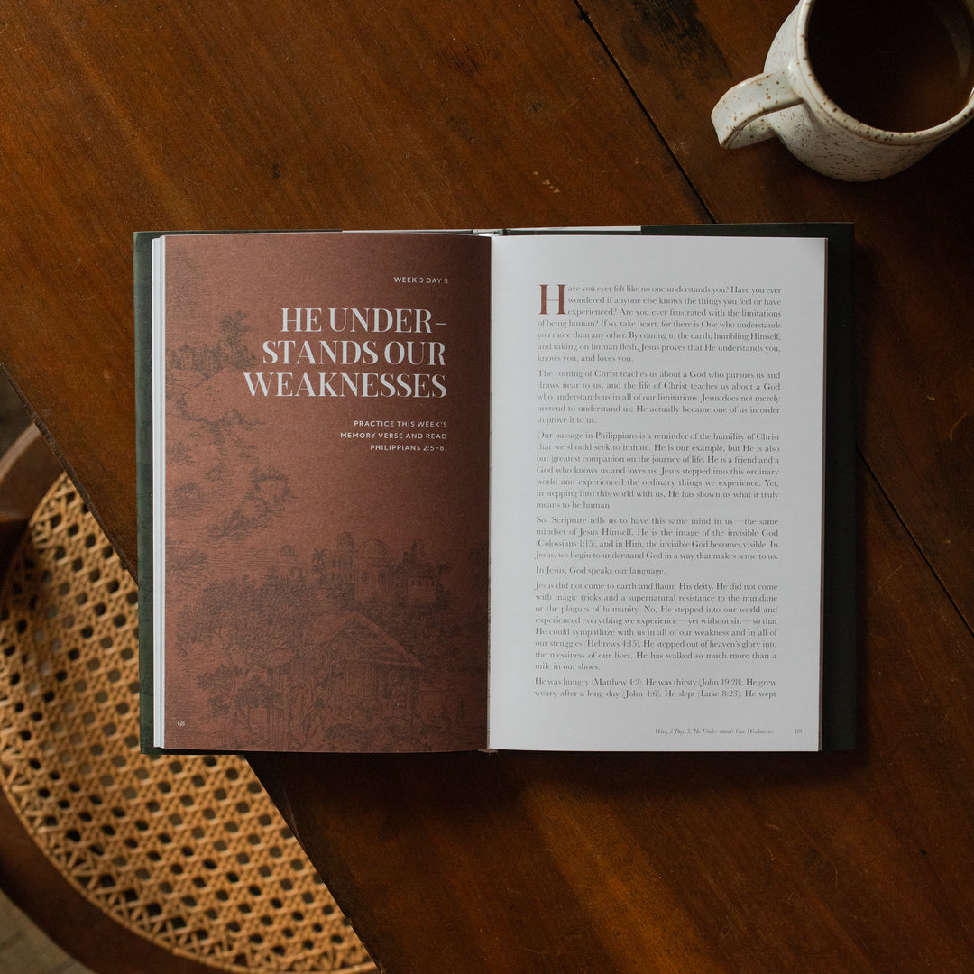 The Immanuel Hardcover opened to the week 3 Day 5 page on a wooden table next to a coffee cup