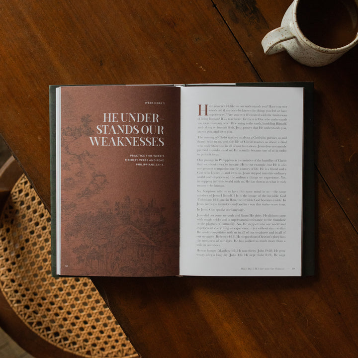 The Immanuel Hardcover opened to the week 3 Day 5 page on a wooden table next to a coffee cup