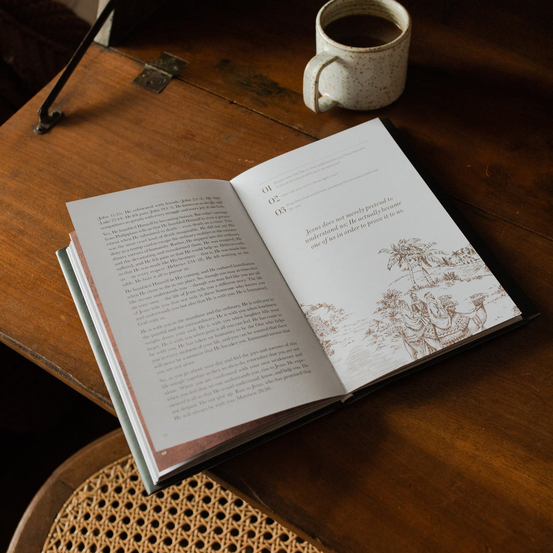 The Immanuel Hardcover opened to the questions and applications on a wooden table next to a coffee cup