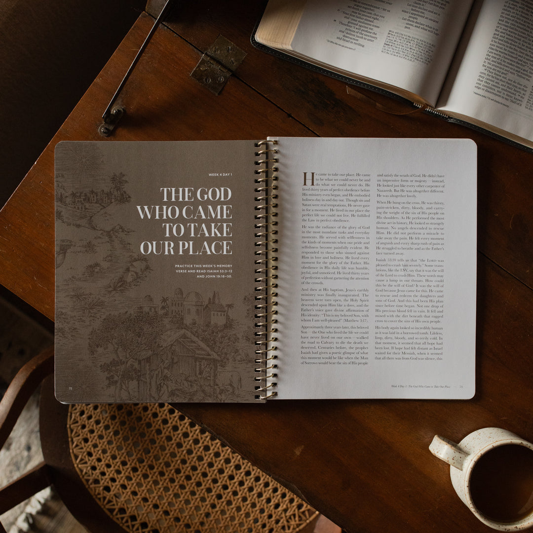 The Immanuel Spiral cover opened to the week 4 Day 1 page on a wooden table near an open bible and a coffee cup