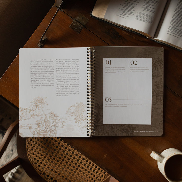 The Immanuel Spiral cover opened to the week 4 applications and questions page on a wooden table near an open bible and a coffee cup