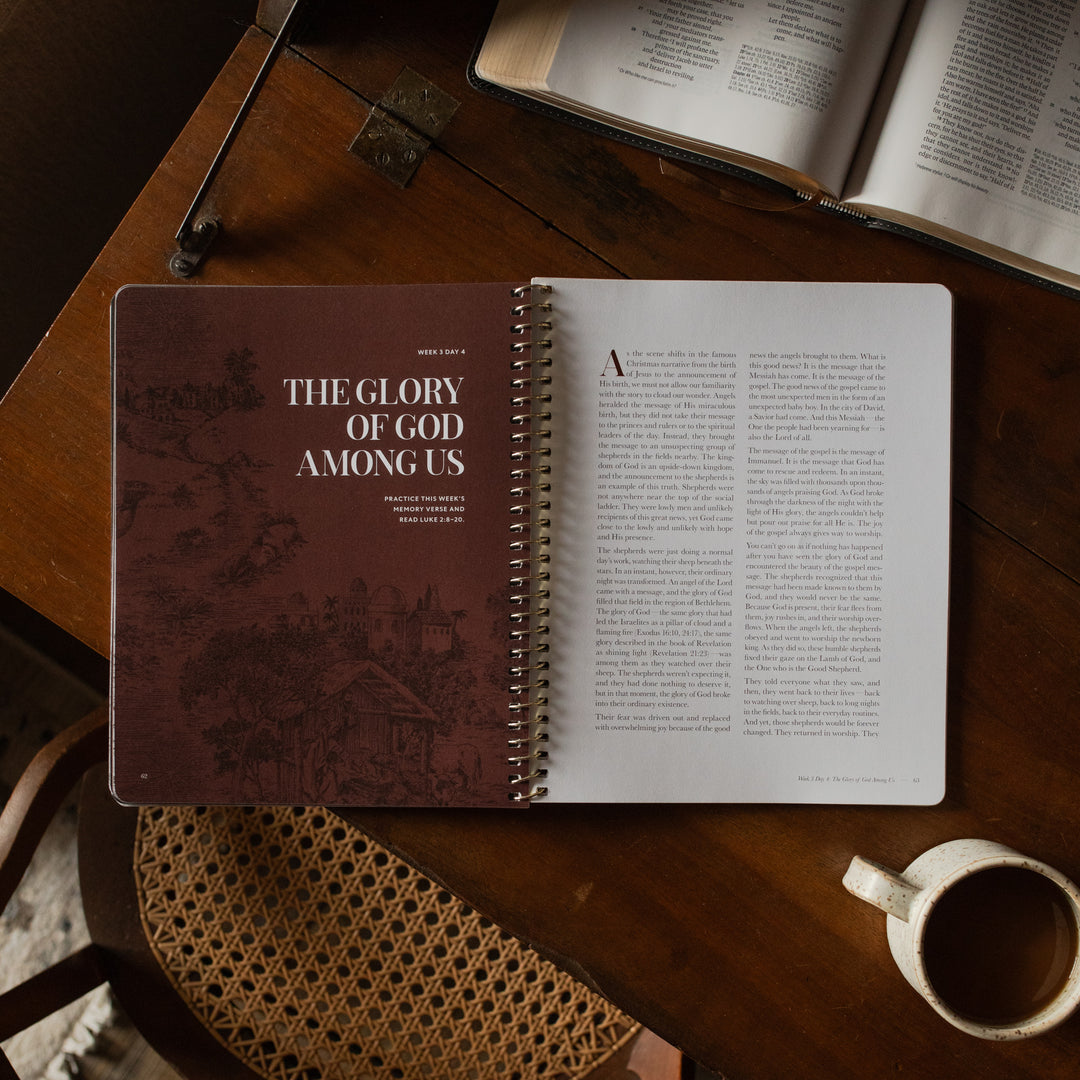 The Immanuel Spiral cover opened to the week 3 day 4 introduction page on a wooden table near an open bible and a coffee cup