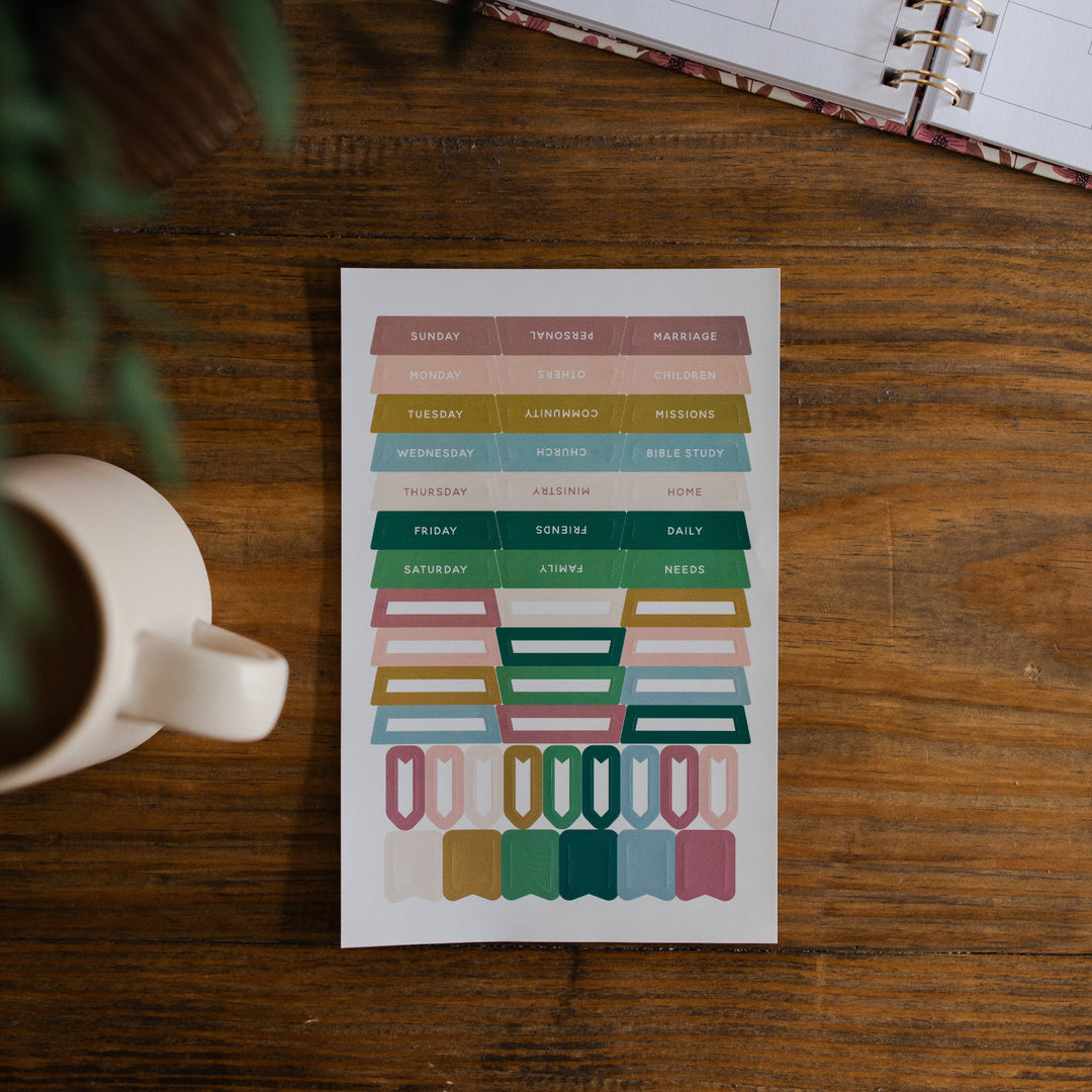 In Everything Journal Sticker Sheet on a brown wooden table next to a white coffee cup and some greenery