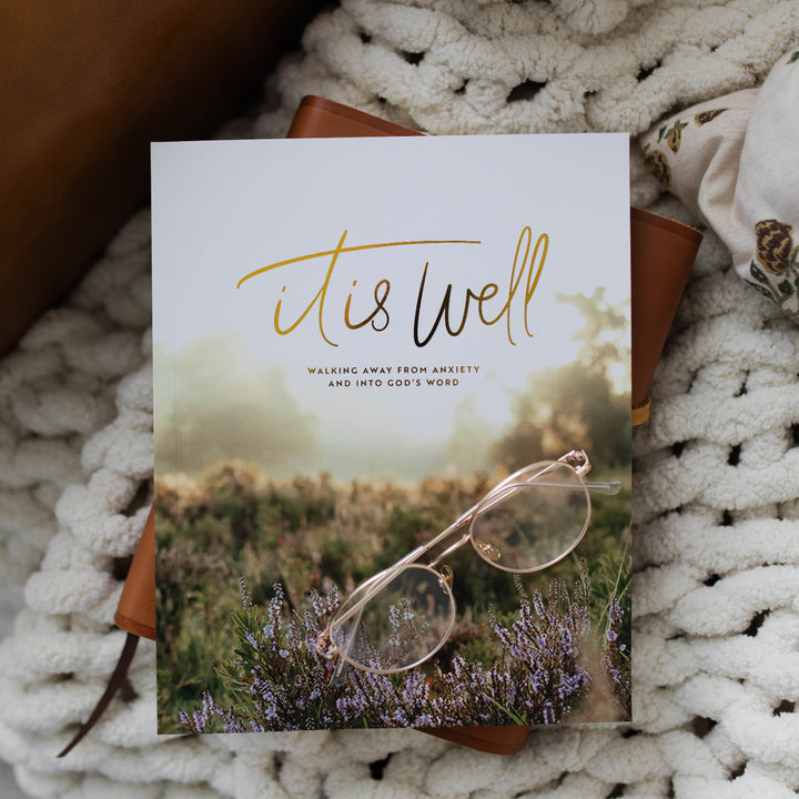 It Is Well Study Cover with a pair of glasses on it; The Study is laying on a leather book resting on a white knitted blanket