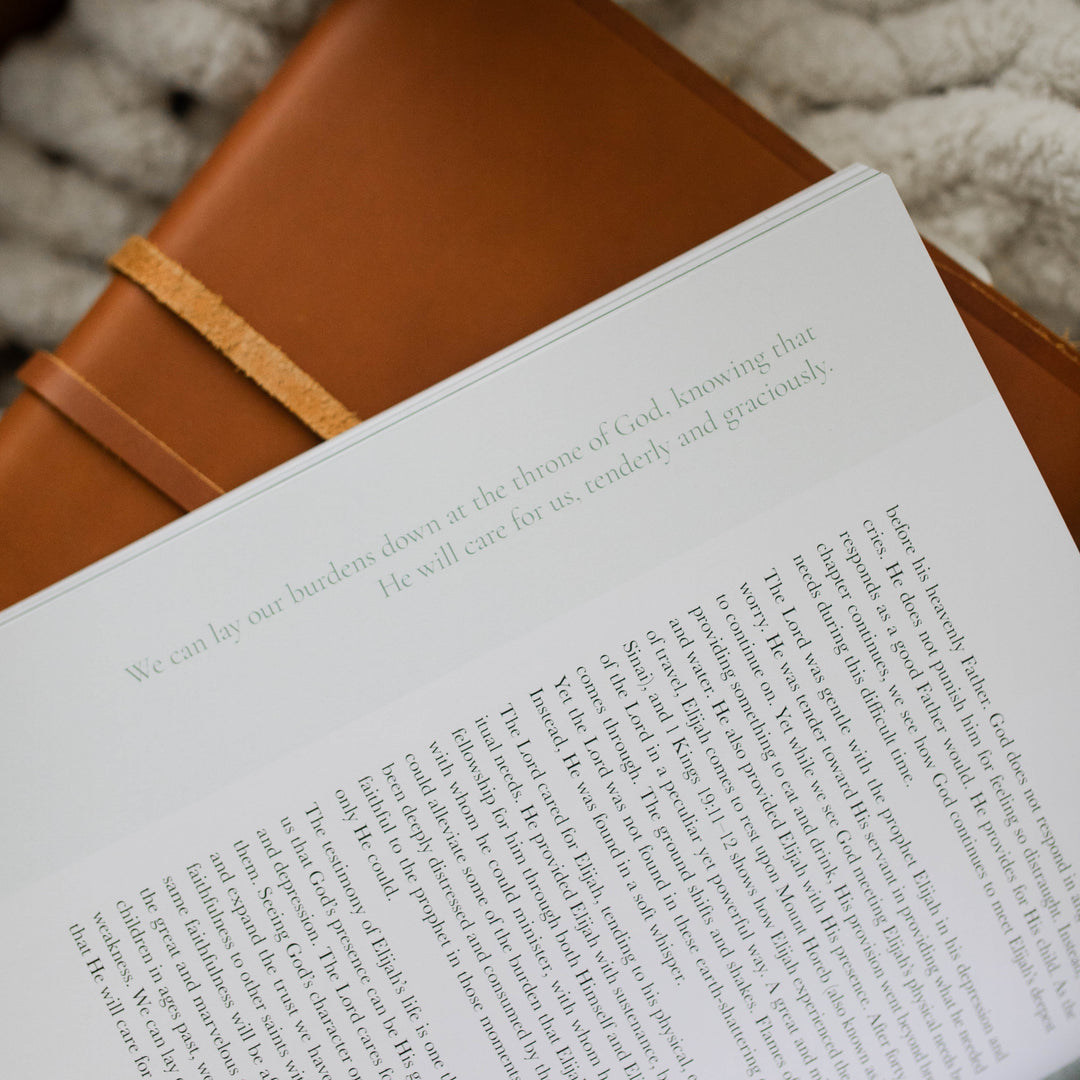 It Is Well Study opened to a up close corner of a page about laying burdens down to God; The study is laying on a leather book and a white knitted blanket