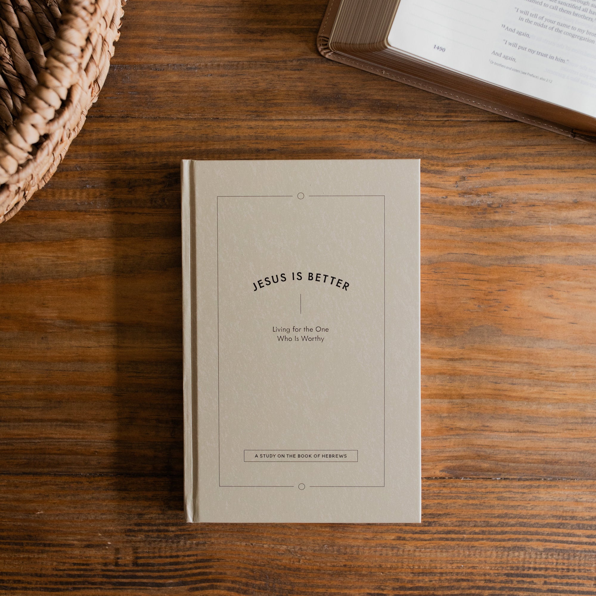 Jesus is Better Mens study cover on a wooden desk next to a woven basket and an open bible