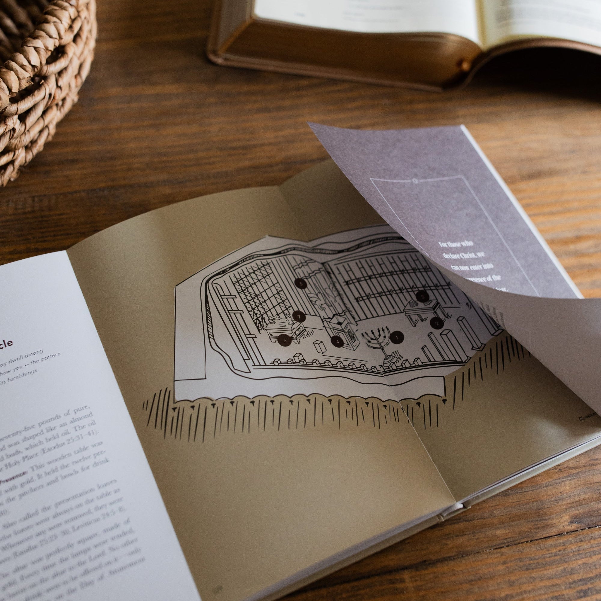 Jesus is Better Mens study opened to the inside of the tabernacle page as it the page is being flipped on a wooden desk next to a woven basket and an open bible