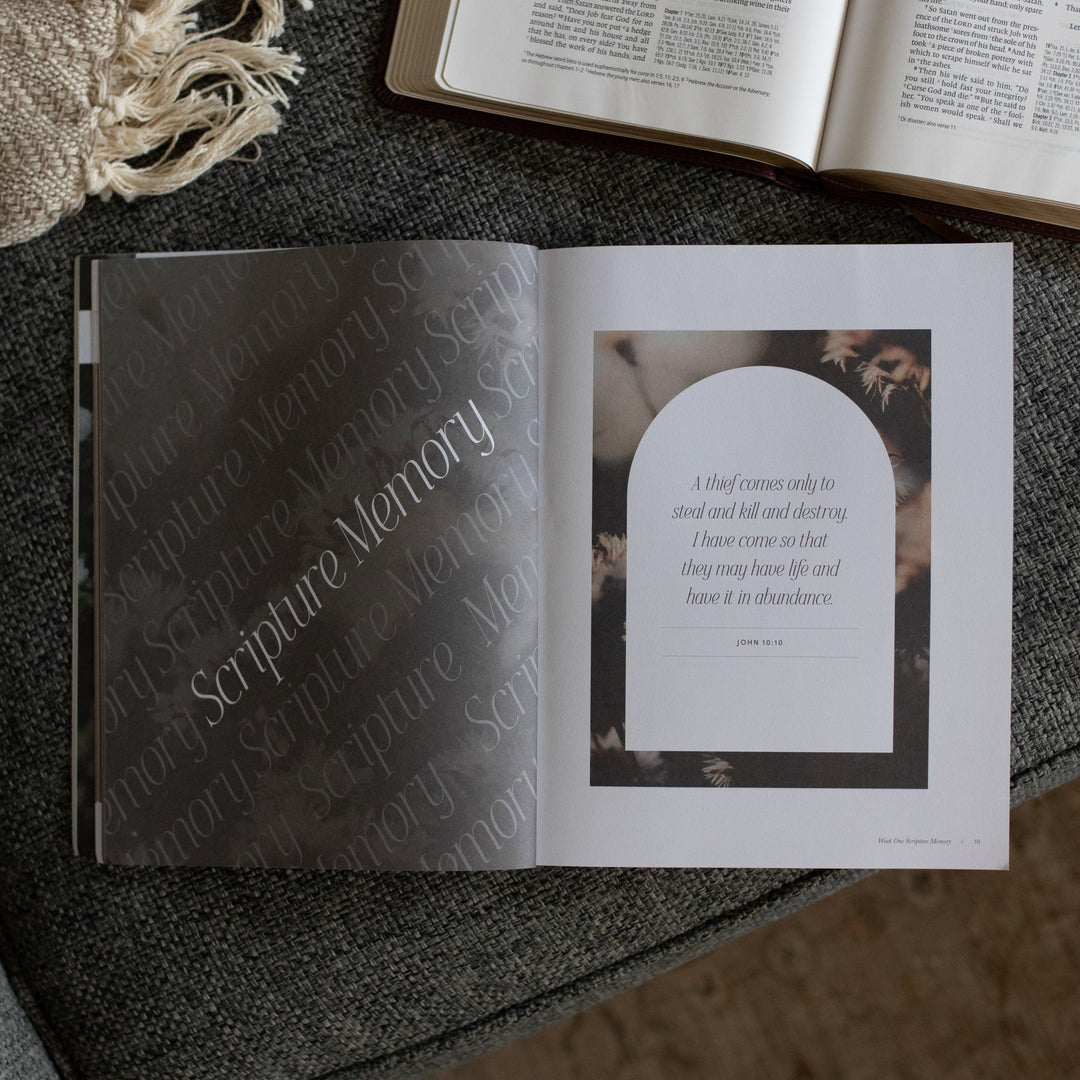 The Job study opened to the scripture memory page near an open bible on a grey couch