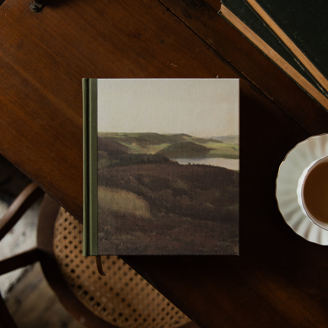 A Bible with a scenic cover on a wooden table next to a cup of coffee