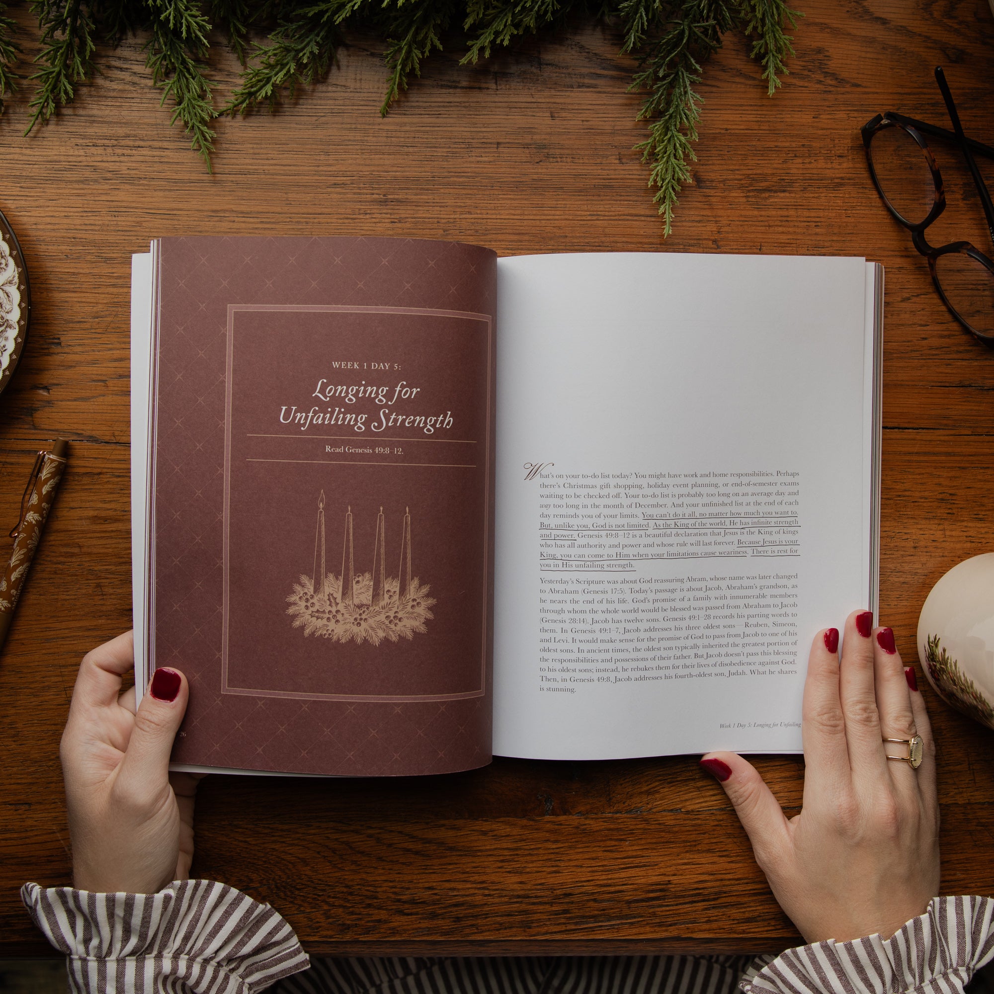 An open book held by two hands with red painted fingernails, placed on a wooden table. The left page shows a brown cover with the title 'Longing for Unfailing Strength' and a candle illustration, while the right page contains printed text.