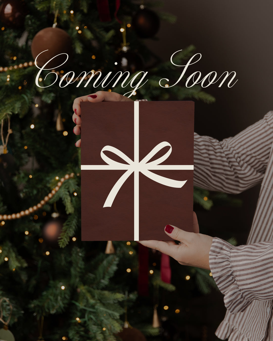 A person in a striped shirt holds a dark brown gift box with a white ribbon and bow in front of a decorated Christmas tree. The words 'Coming Soon' appear in white script across the top.