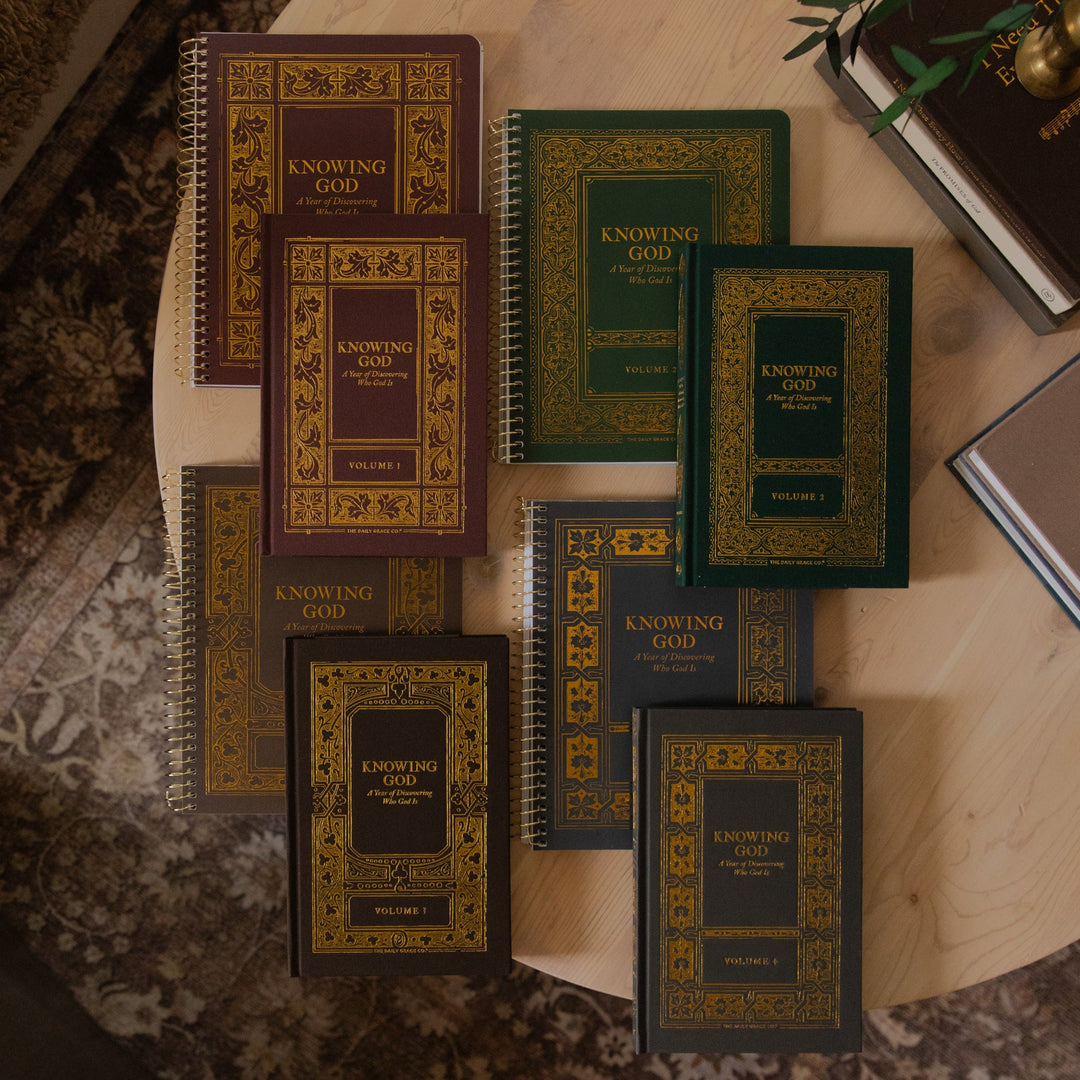 A set of spiral-bound books titled 'Knowing God' arranged on a round wooden table. The books have ornate gold-embossed covers in dark brown, green, and black, with some showing gold and others showing silver spiral binding.