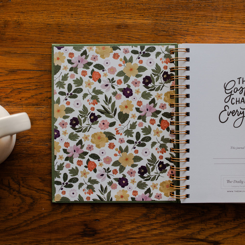 The Gospel Changes Everything Not taking Journal opened to the front cover on a wooden table next to a coffee cup