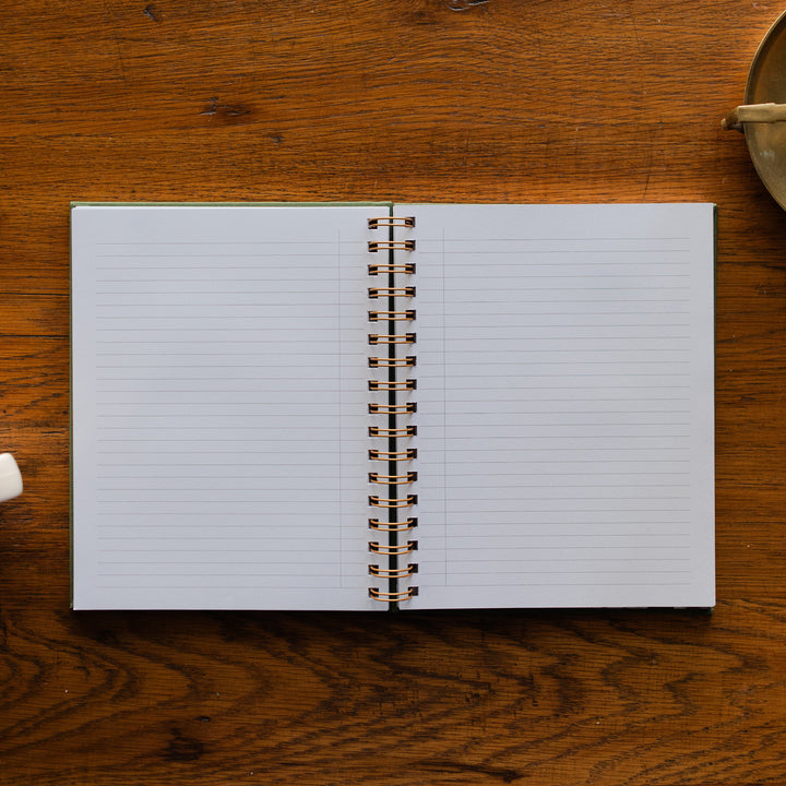 The Gospel Changes Everything Not taking Journal opened to its sample pages on a wooden table next to a bronze oil lamp