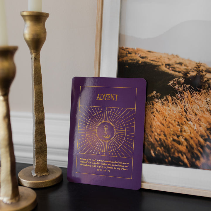 A Purple Advent card from the Liturgical Living Display Card leaning against a painting and near candlesticks