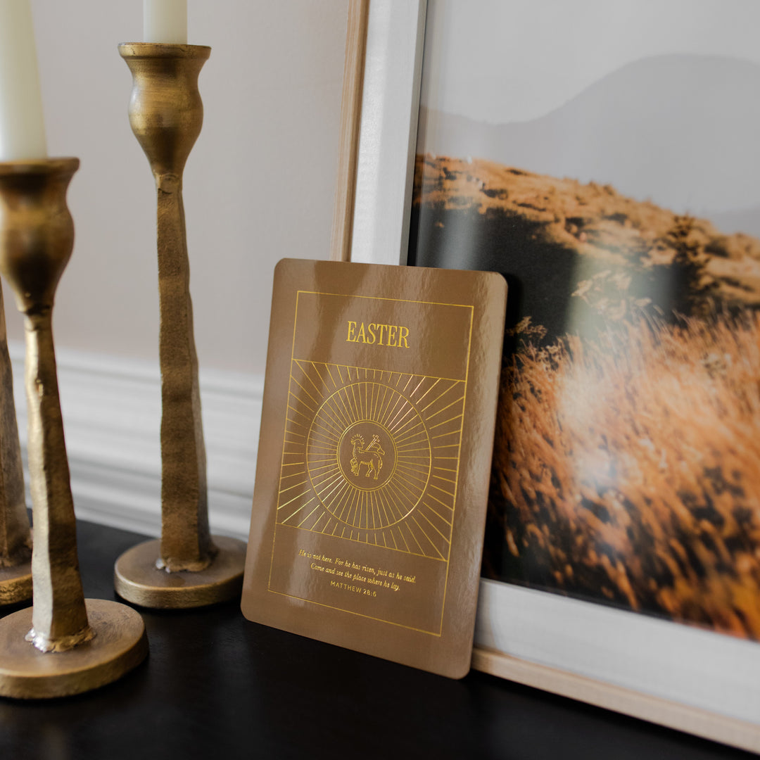 A Brown Easter card from the Liturgical Living Display Card leaning against a painting and near candlesticks
