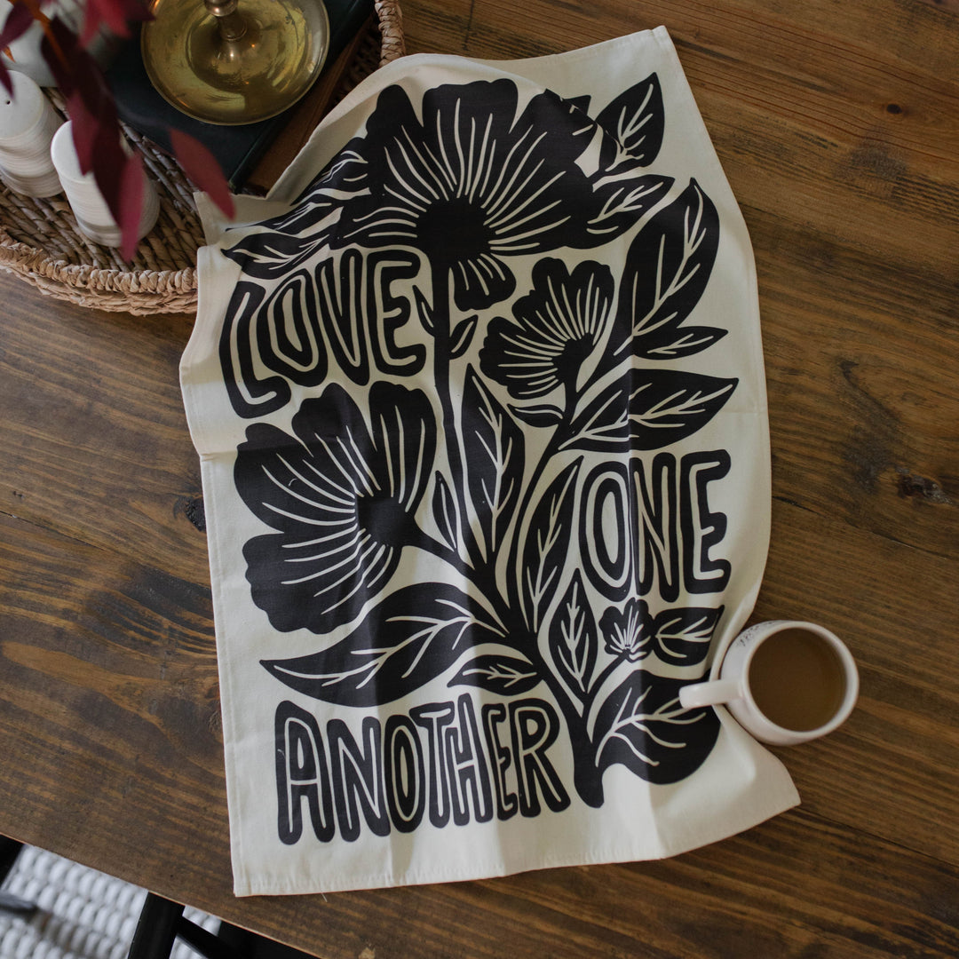 Love One Another Christian tea towel with floral pattern open on a table