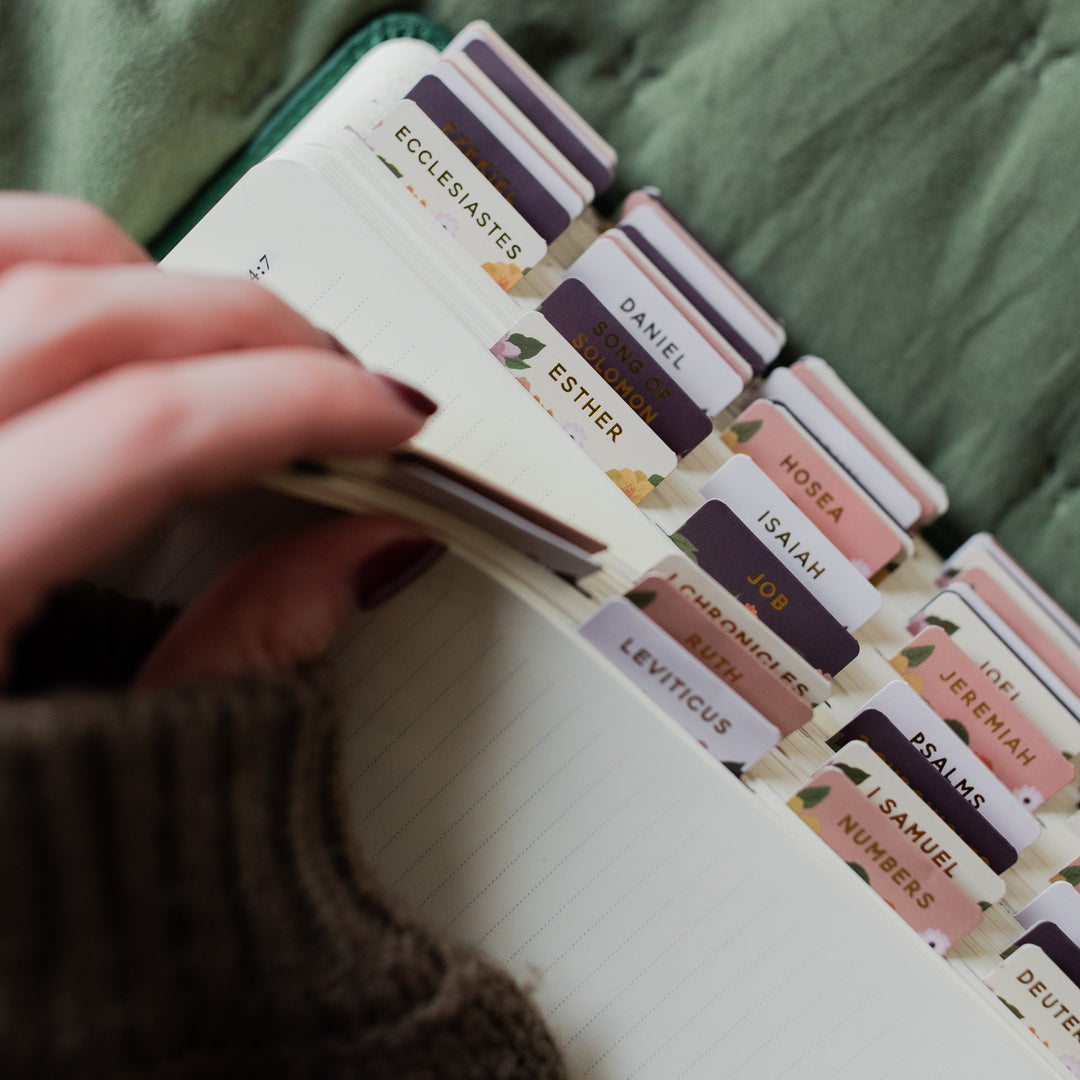 Hand holding a book with colorful tabs labeled with Bible chapter names.