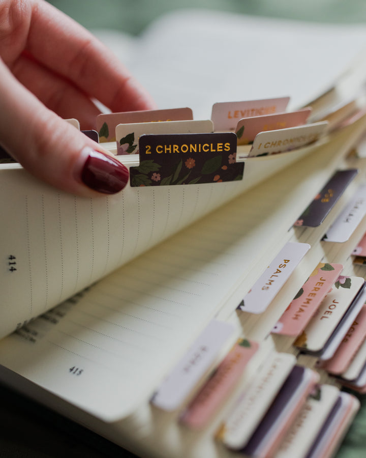 Hand holding a book with colorful tabs labeled with Bible verses