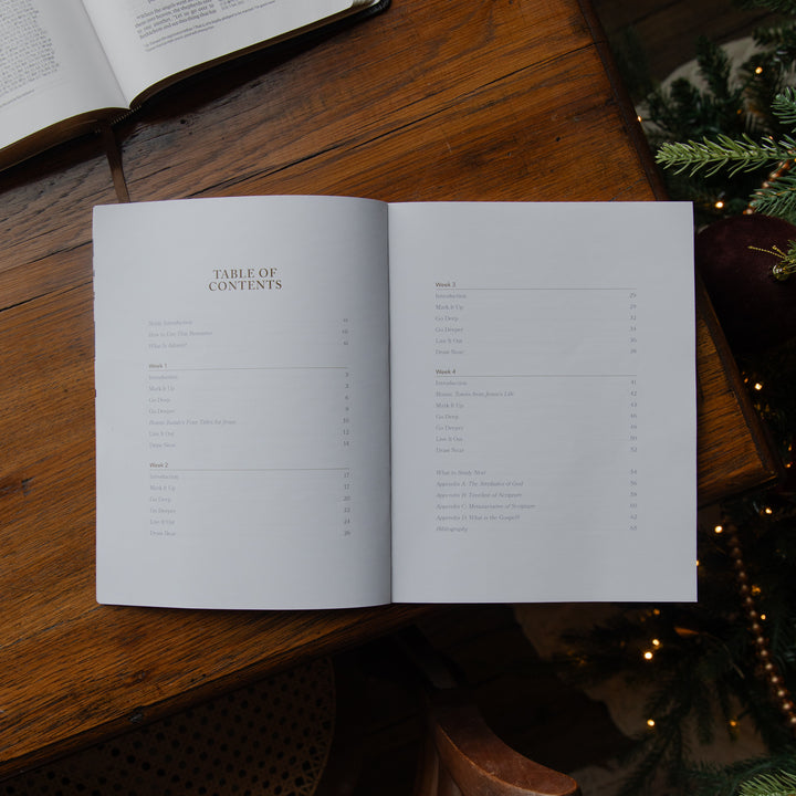 An open book showing the Table of Contents on a rustic wooden table, with an open book and holiday decorations visible in the background.