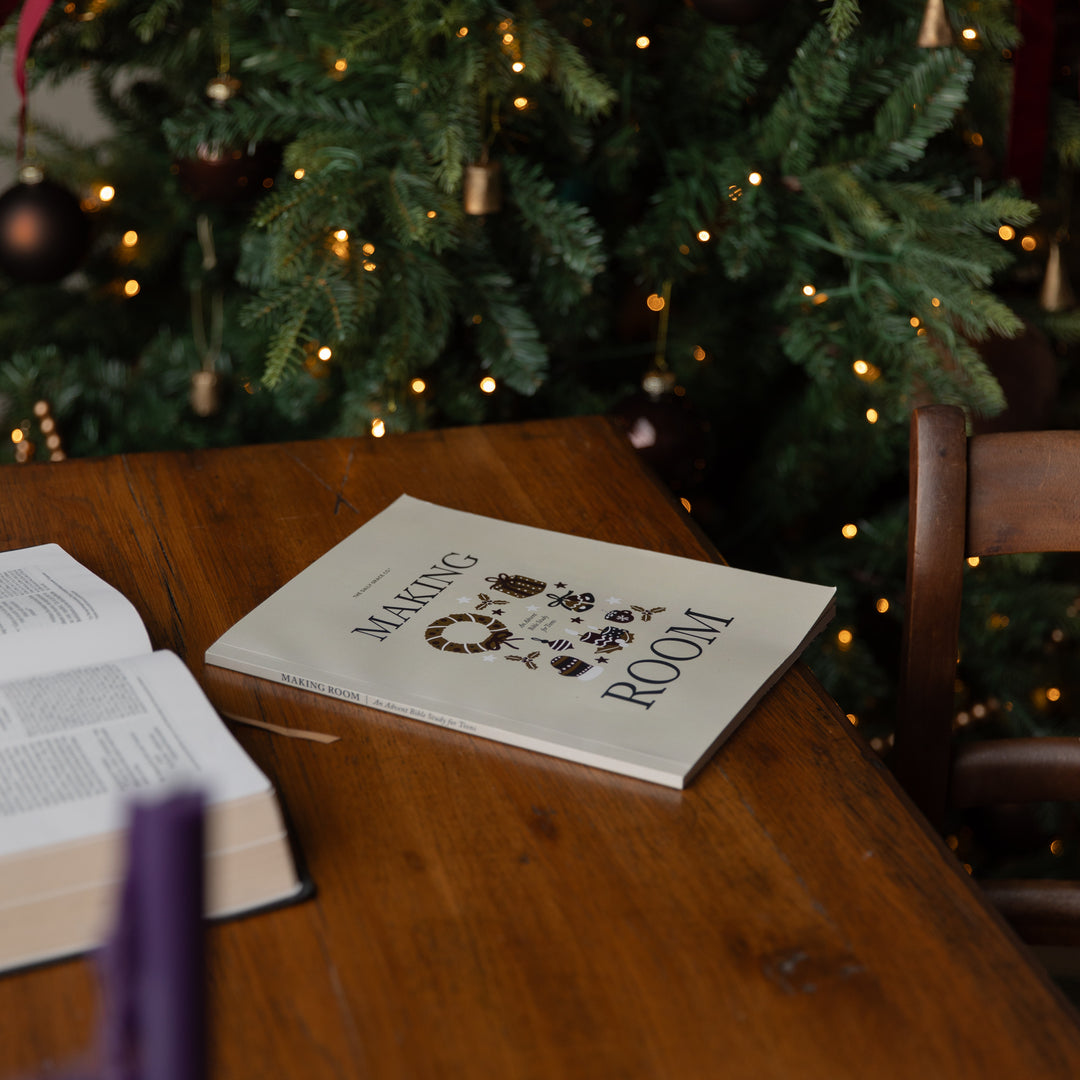 A book titled 'Making of Our Room' lies open on a wooden table in a cozy room setting, with a decorated Christmas tree glowing in the background.