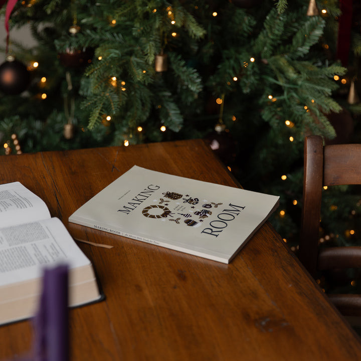 A book titled 'Making of Our Room' lies open on a wooden table in a cozy room setting, with a decorated Christmas tree glowing in the background.