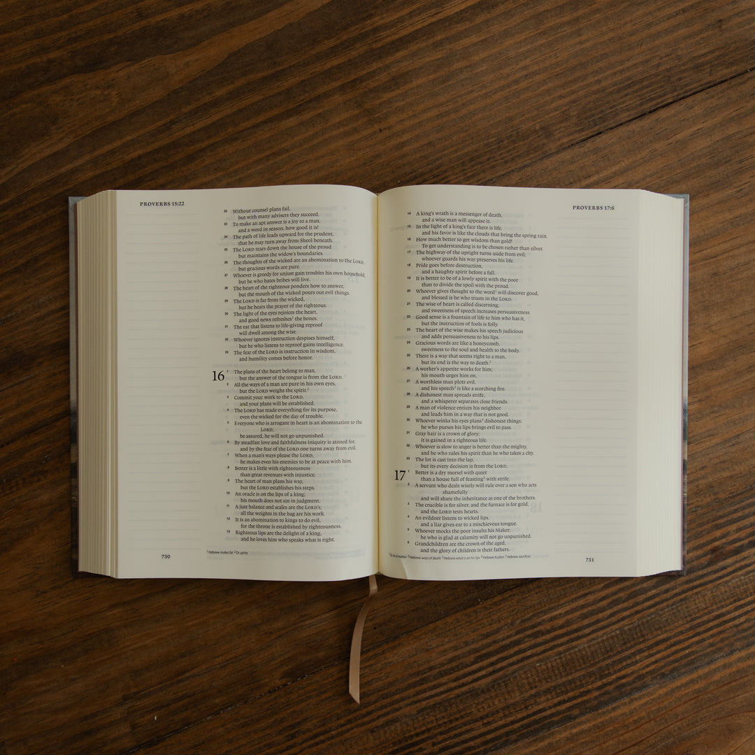 An open book showing printed text pages, placed on a dark wood tabletop. A ribbon bookmark hangs from the bottom center.
