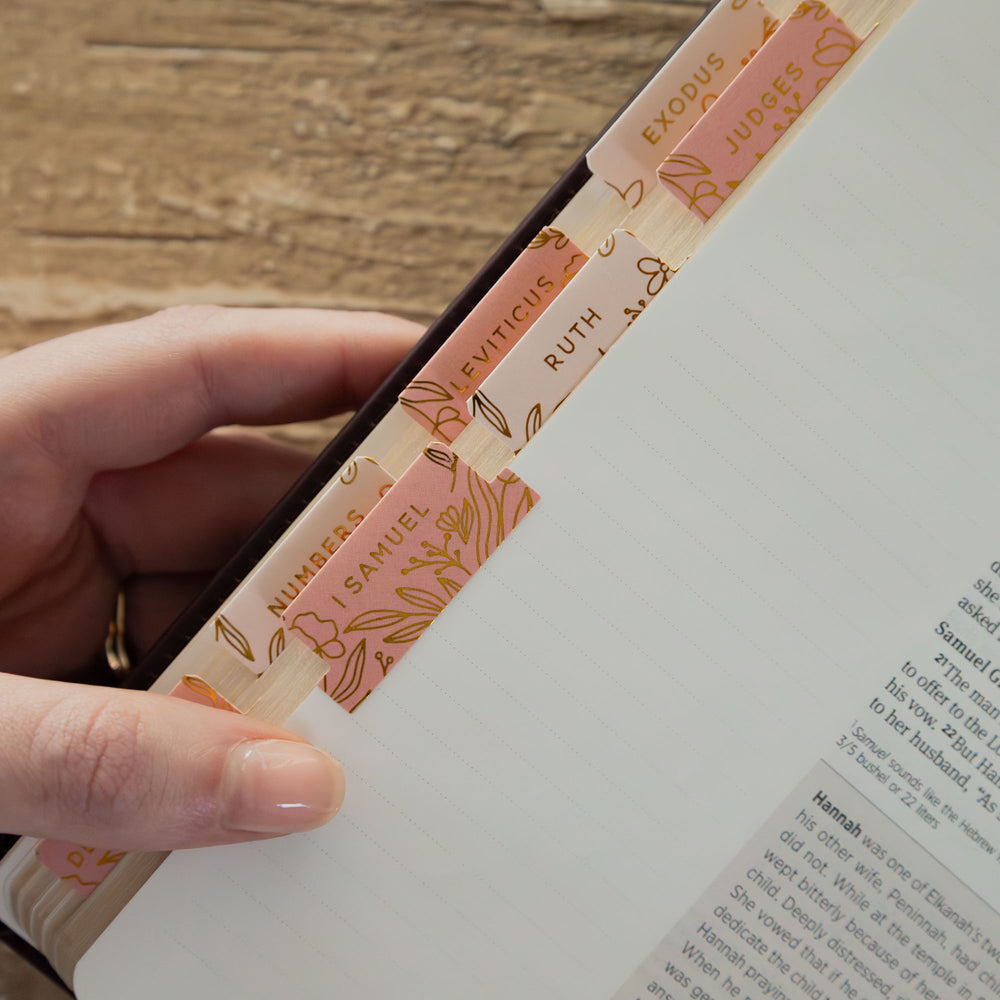 Hand holding a book with decorative pink and gold page markers on a wooden surface