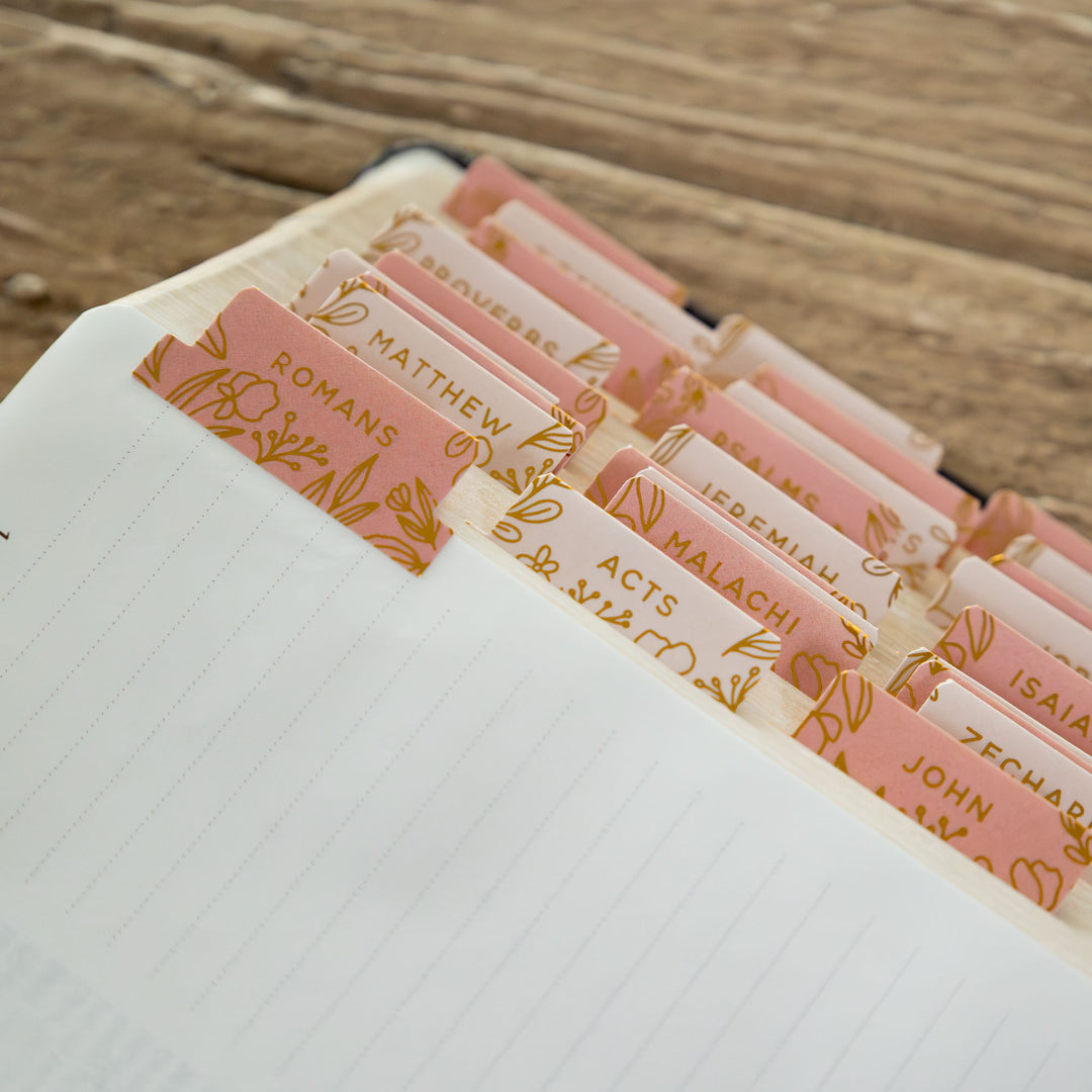 Book with pink and gold bookmark markers for Bible chapters on a wooden surface