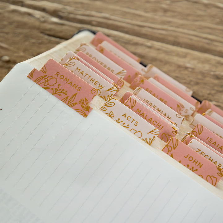 Book with pink and gold bookmark markers for Bible chapters on a wooden surface