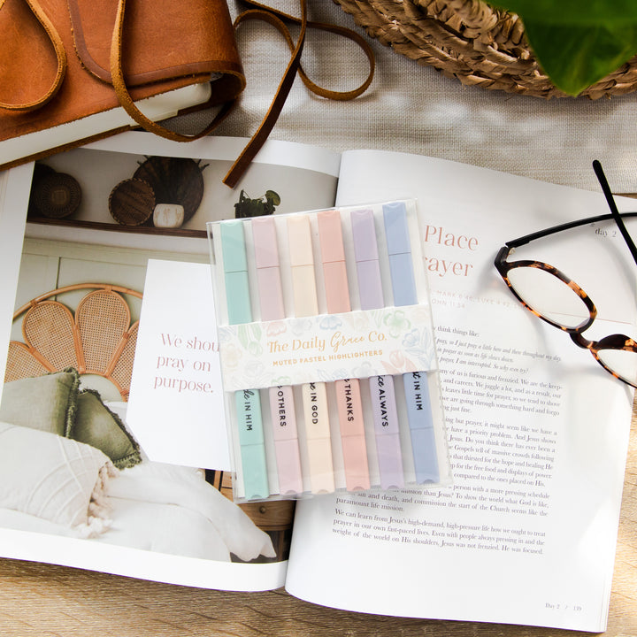 A package of Muted Pastel Highlighters are resting on top of an open Bible study next to a Bible and a pair of glasses. 