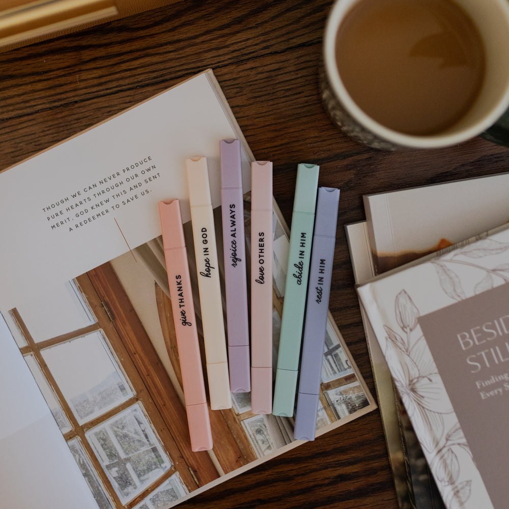Stack of colorful Bible highlighters on a book with a cup of coffee nearby