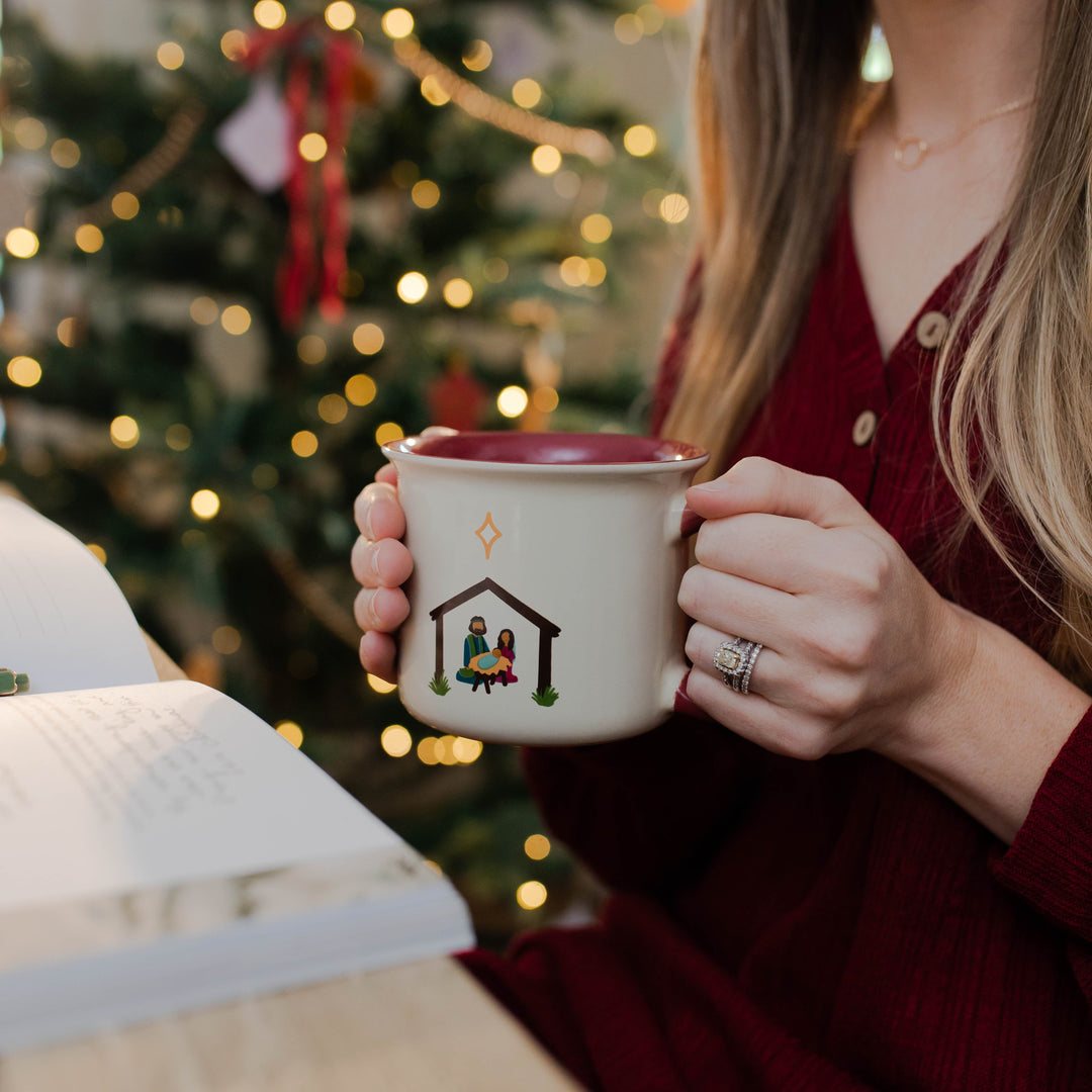 Christian woman holding Christmas Nativity Mug with family devotional on the table