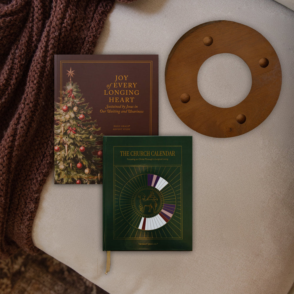 The Advent study, church calendar and the advent candle ring on a couch cushion near a maroon colored blanket