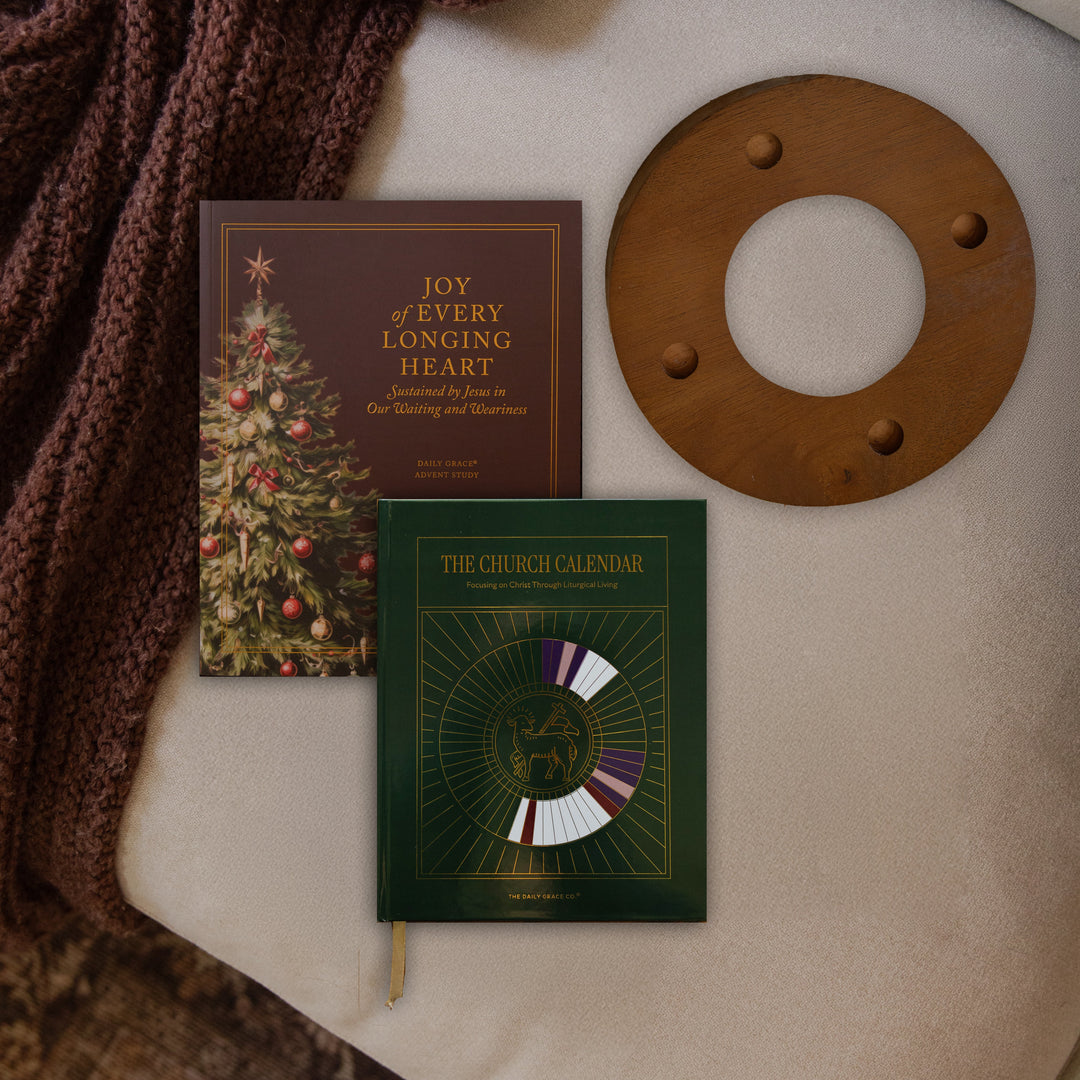 The Advent study, church calendar and the advent candle ring on a couch cushion near a maroon colored blanket